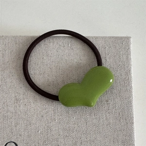 Detailaufnahme der grünen herzförmigen Haarspange mit glänzender Oberfläche und schwarzem Gummiband