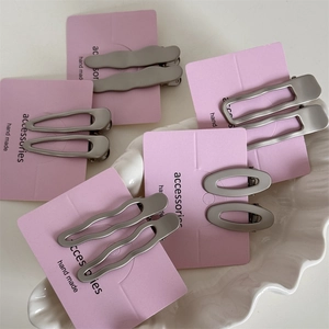 Vue macro de barrettes géométriques en argent mat sur des cartes de présentation roses