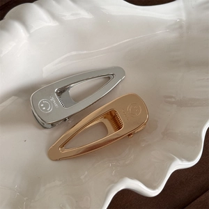 Polished gold and silver minimalist metal hair clips with smile engraving on ceramic tray