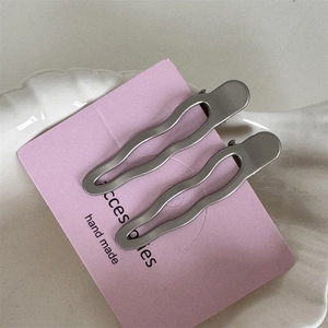 Gros plan de deux barrettes à cheveux ondulées argent mat sur carte rose