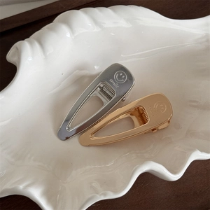 Elegant gold and silver teardrop smile hair clips displayed on a white shell plate
