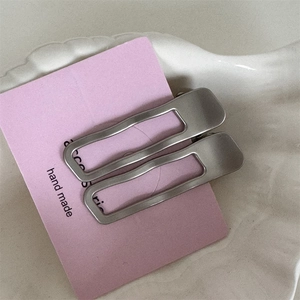 Détail macro de pinces à cheveux argentées mates avec bords ondulés sur carte rose