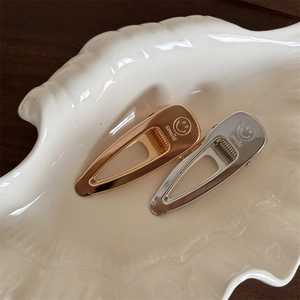 Close-up of gold and silver teardrop hair clips with smile engraving on shell tray