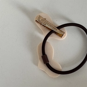 Detail von cremefarbener Herz-Haarklammer mit Goldclip und schwarzem Haargummi