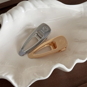 Detailed view of silver and gold metal hair clips with engraved smile icons in shell tray