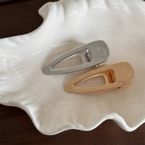 Minimalist gold and silver teardrop hair clips with smile engraving in ceramic dish