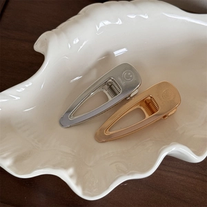 Detail view of gold and silver teardrop hair clips with smile engraving on shell tray