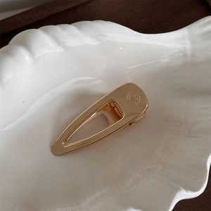 Close-up of golden metal teardrop hair clip featuring engraved smile icon and smile text
