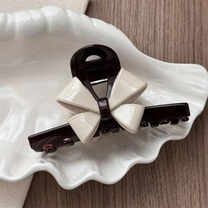 Detailed close-up of dark brown hair claw with elegant cream 3D bow on a shell tray