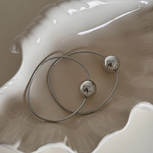 Detail of silver metallic sphere hair tie on white shell tray with mirror finish texture