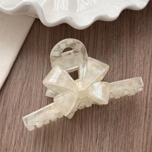 Detail showing the glossy acetate bow hair claw clip with iridescent finish and brand logo