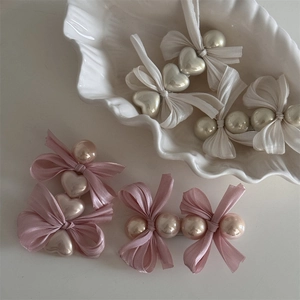 Set aus rosa Haarklammern mit Schleifen, Perlen und Herzen auf einer weißen Schale