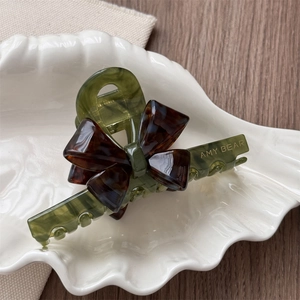 Detail view of olive green acetate hair claw with tortoiseshell bow on white shell tray