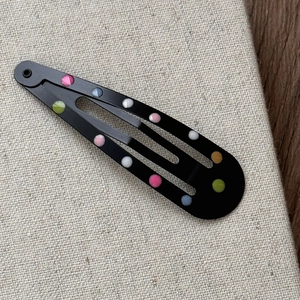 Détail de barrettes à cheveux en métal noir avec un motif à pois colorés vibrants