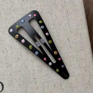Détail d'une barrette triangle noire avec des pois colorés en émail sur un support texturé