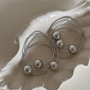 Close-up of silver elastic hair ties with three mirror-finish metallic spheres on tray