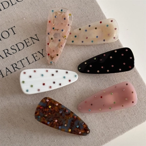 Détail de six pinces à cheveux goutte avec strass colorés sur fond en lin texturé