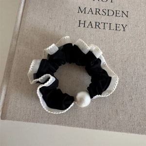 Close-up of a black scrunchie with white lace trim and a large pearl ornament on a book
