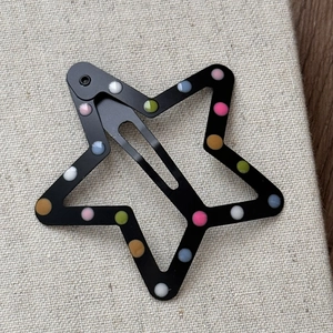 Détail d'une pince à cheveux étoile en métal avec pois colorés sur fond noir