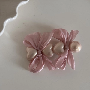 Detail der rosa Satin-Schleifen-Haarklammer mit herzförmigen Perlen auf weißem Grund