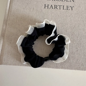 Detail of a ruffled fabric hair tie in black and white, featuring soft layered textures