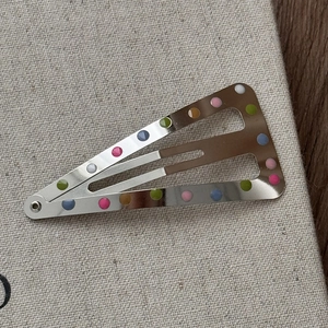 Détail d'une pince à cheveux en métal avec pois colorés sur toile beige