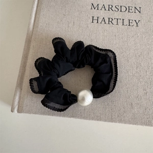 Close-up of black lace scrunchie with a large faux pearl on a textured book cover