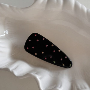 Détail d'une pince à cheveux noire avec strass colorés sur une coupelle en coquillage