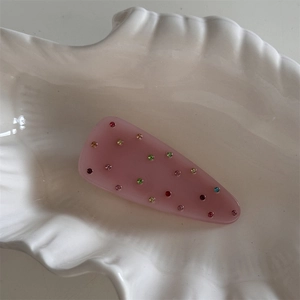 Détail d'une pince à cheveux rose en résine avec strass colorés sur une assiette coquille