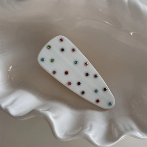 Détail de pince à cheveux effet marbre avec strass multicolores sur un plat coquillage