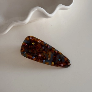 Détail macro de la pince à cheveux en acétate avec strass colorés sur plateau blanc