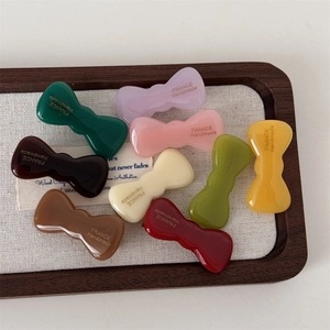 Handmade acetate bow hair clips in assorted colors on a wooden display tray