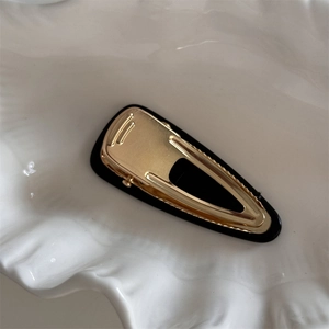 Gros plan d'une barrette à cheveux goutte dorée et noire sur un plateau coquillage