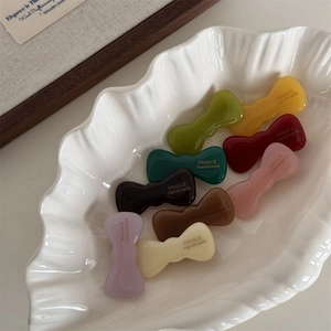 Elegant wavy bow acetate hair clips set in nine assorted colors on a shell plate