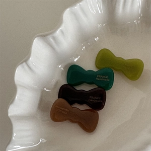 Detail of four acetate bow hair clips in green and brown tones on a white plate