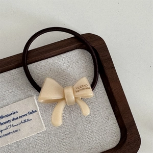 Macro detail of cream acetate bow hair tie with handmade gold logo on elastic rope