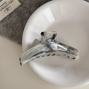 Detail view of ink marble pattern acetate hair claw clip on elegant ceramic tray
