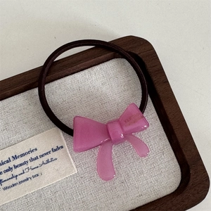 Pink acetate bow hair tie with pearl texture on a wooden jewelry display tray