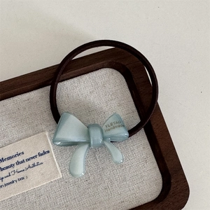 Detail of blue acetate bow hair tie with handmade gold lettering on a wooden tray