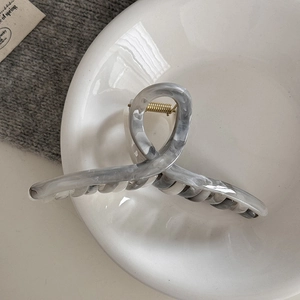 Macro shot of ink marble claw clip with gold spring in a minimalist ceramic dish setting