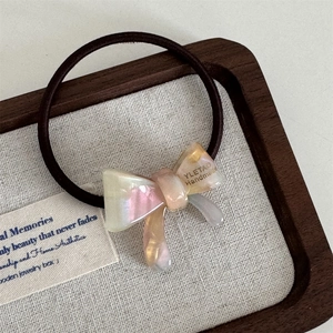 Detail of handmade acetate bow hair tie with pearlescent finish on wooden tray