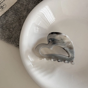 Detailed macro view of heart-shaped ink marble pattern hair claw on a ceramic plate