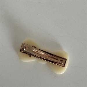 Detailed view of copper-tone metal alligator hair clip with cream acetate bow