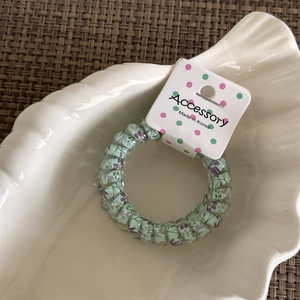 Detailed view of light green floral spiral hair coil tie on a decorative shell plate
