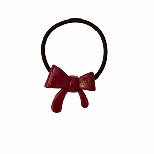 Elastic hair tie with a shiny red resin bow and gold logo detail on a white background