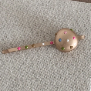 Close-up of golden barrette with colorful enamel dots on a fabric textured background
