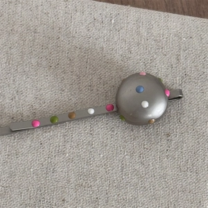 Detail of a silver metal hair clip with colorful polka dots on a round decorative disc