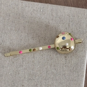 Macro shot of gold metal hair clip featuring colorful polka dots and a spherical detail
