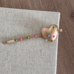 Close-up of golden heart hairpin with colorful polka dots on rustic linen surface