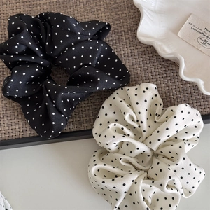 Close-up of black and white polka dot satin scrunchies set on a woven mat